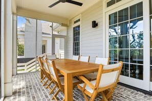 A covered patio with a wooden table and chairs, large windows, and a ceiling fan. - New Oceanfront Jekyll Home • Beach Boardwalk • Fireplace Porch (Jekyll Island)