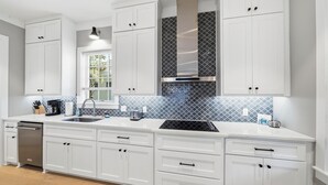 A modern kitchen with white cabinetry, a stainless steel dishwasher, a double sink, and a patterned backsplash. - New Oceanfront Jekyll Home • Beach Boardwalk • Fireplace Porch (Jekyll Island)