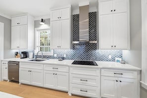 A modern kitchen with white cabinetry, a stainless steel dishwasher, a double sink, and a patterned backsplash.