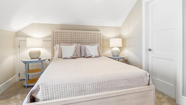 A bedroom with a bed, two bedside tables, a headboard, and a door. - New Oceanfront Jekyll Home • Beach Boardwalk • Fireplace Porch (Jekyll Island)