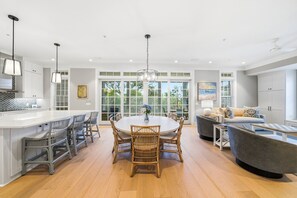 A spacious kitchen with a central island, dining area with wicker chairs, and a large window providing natural light. - New Oceanfront Jekyll Home • Beach Boardwalk • Fireplace Porch (Jekyll Island)