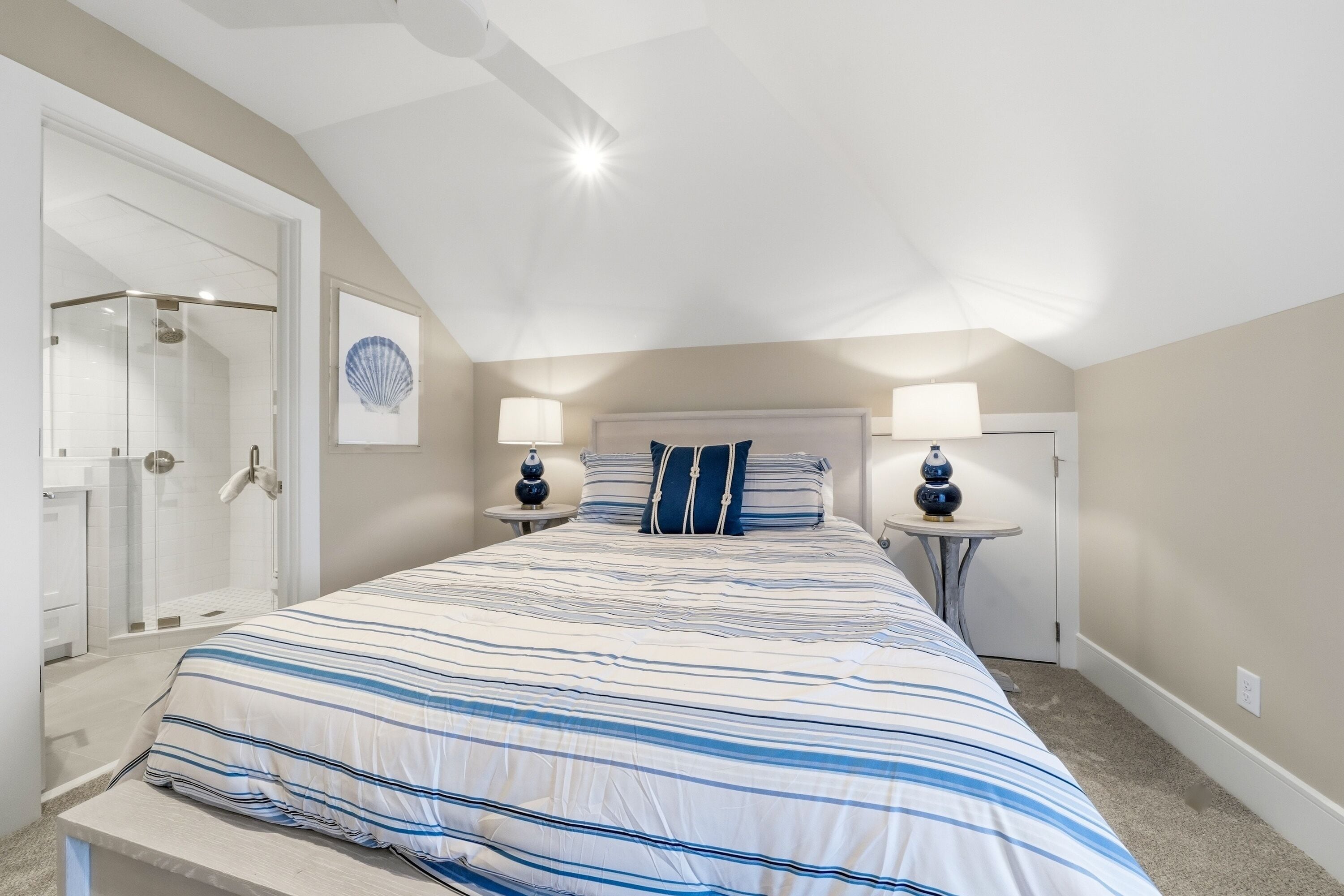 A bedroom with a large bed, two bedside tables with lamps, a shower, and a door leading to another room.