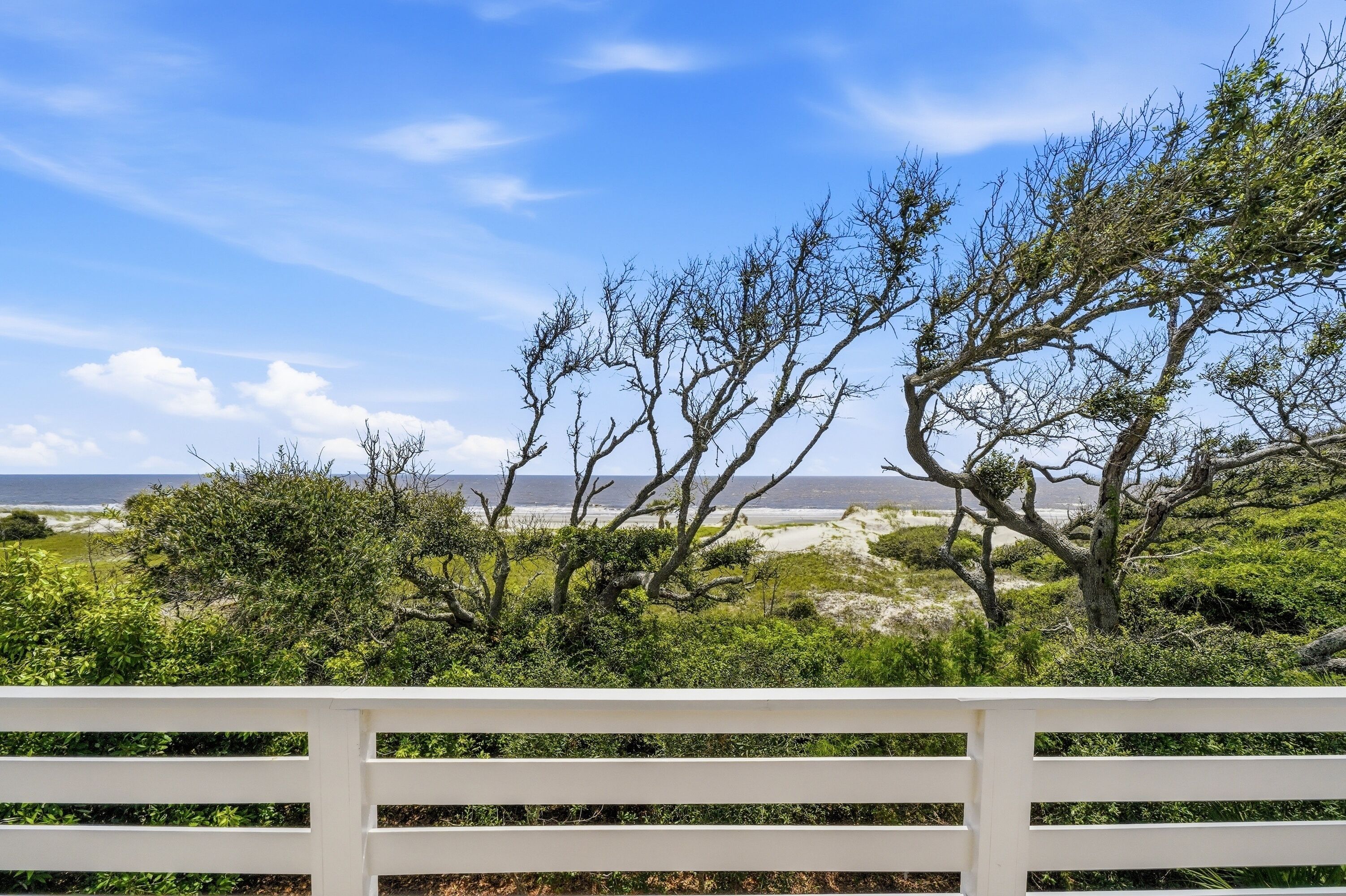 Cerca branca com vista para a praia e árvores ao fundo.