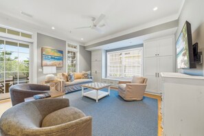 Ein geräumiges Wohnzimmer mit großem Fenster, Deckenventilator und flach an der Wand befestigtem Flachbildfernseher.