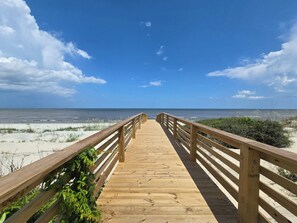 A wooden boardwalk leading to a beach with clear skies. - New Oceanfront Jekyll Home • Beach Boardwalk • Fireplace Porch (Jekyll Island)