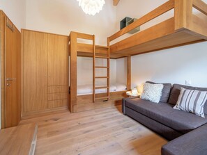 Una cama litera con escalera, un armario, un sofá y una mesita de noche con lámpara.
