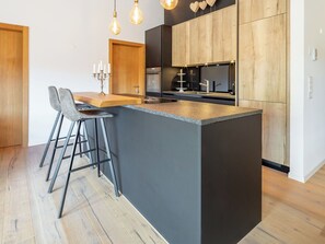 A modern kitchen with a central island, bar stools, and pendant lighting. - Cosy apartment for 5 people with WIFI, TV and balcony (Waldhaus)