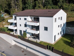 Un edificio residencial moderno de varios pisos, con balcones, techo plano y un césped cuidado.