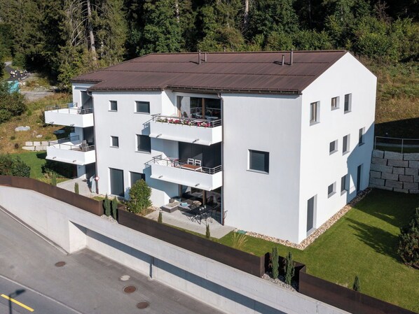 Un edificio residencial moderno de varios pisos, con balcones, techo plano y un césped cuidado.