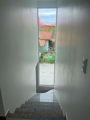 A staircase leading to a balcony with a view of a red-roofed building and a green area. - Lumina Riviera Ferrugem (Garopaba)