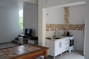 A compact kitchen with a television, a sink, and a stove. - Lumina Riviera Ferrugem (Garopaba)