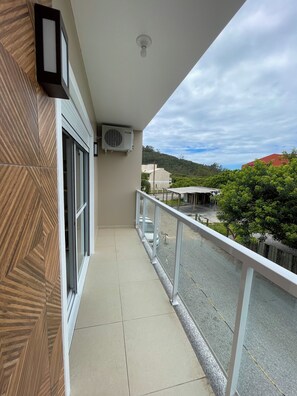 Ein Balkon mit Blick auf eine Straße und Grünflächen, eine Klimaanlage und eine Wand mit Muster.