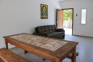 A living room with a wooden coffee table featuring beer-related designs, a dark sofa, and a door leading outside. - Lumina Riviera Ferrugem (Garopaba)