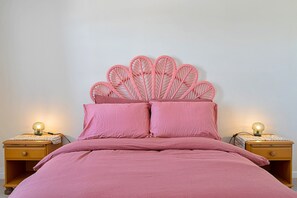 Ein Bett mit rosa Kopfteil und passenden Kissen, flankiert von zwei Nachttischen mit Lampen.