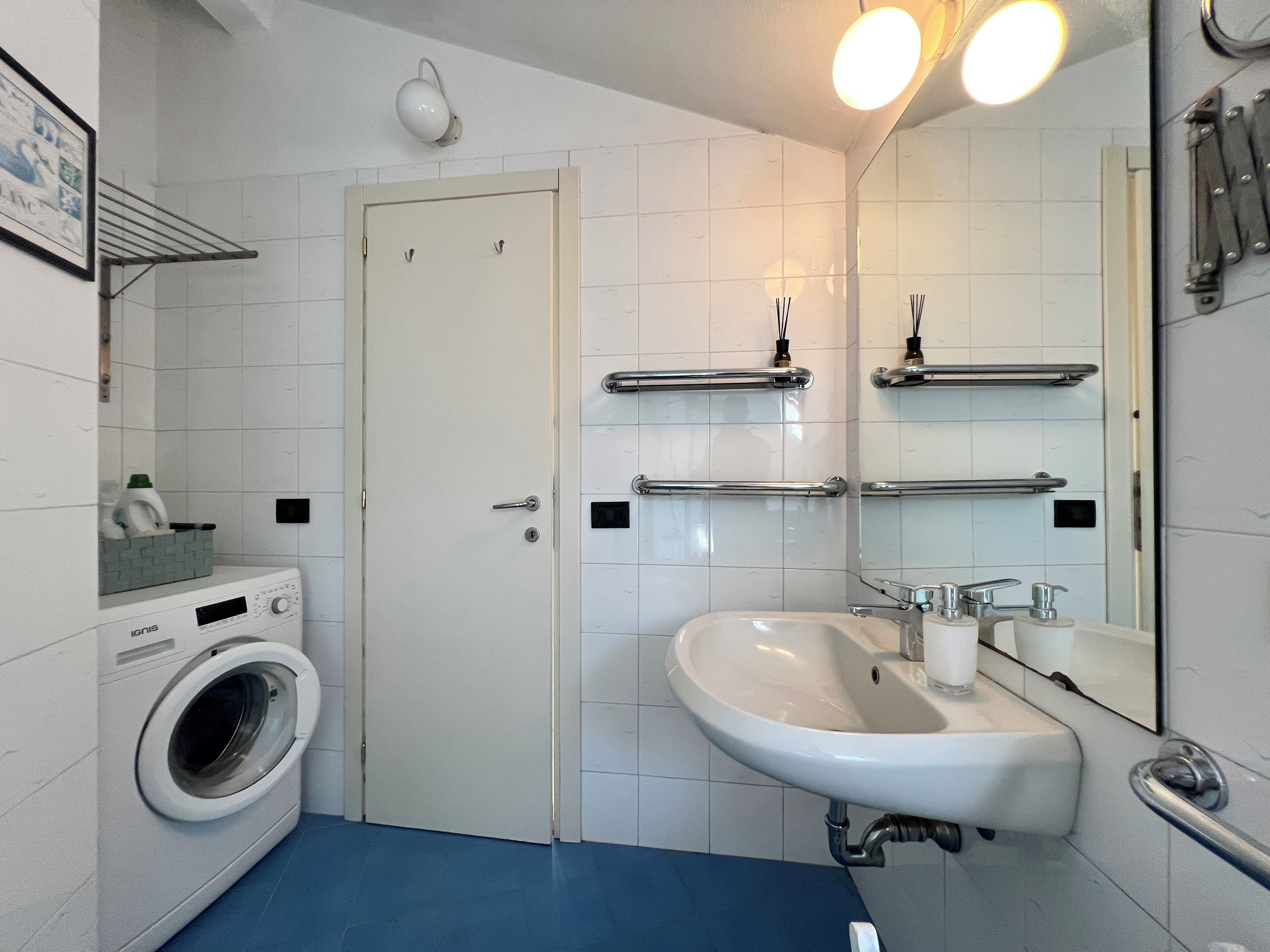 Un baño con lavadora, lavamanos, espejo y perchero para toallas.
