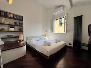 A hotel room with a bed, bedside tables, a bookshelf, an air conditioning unit, a window with a view, and a television. - CASA DEL POZZO (Rapallo)