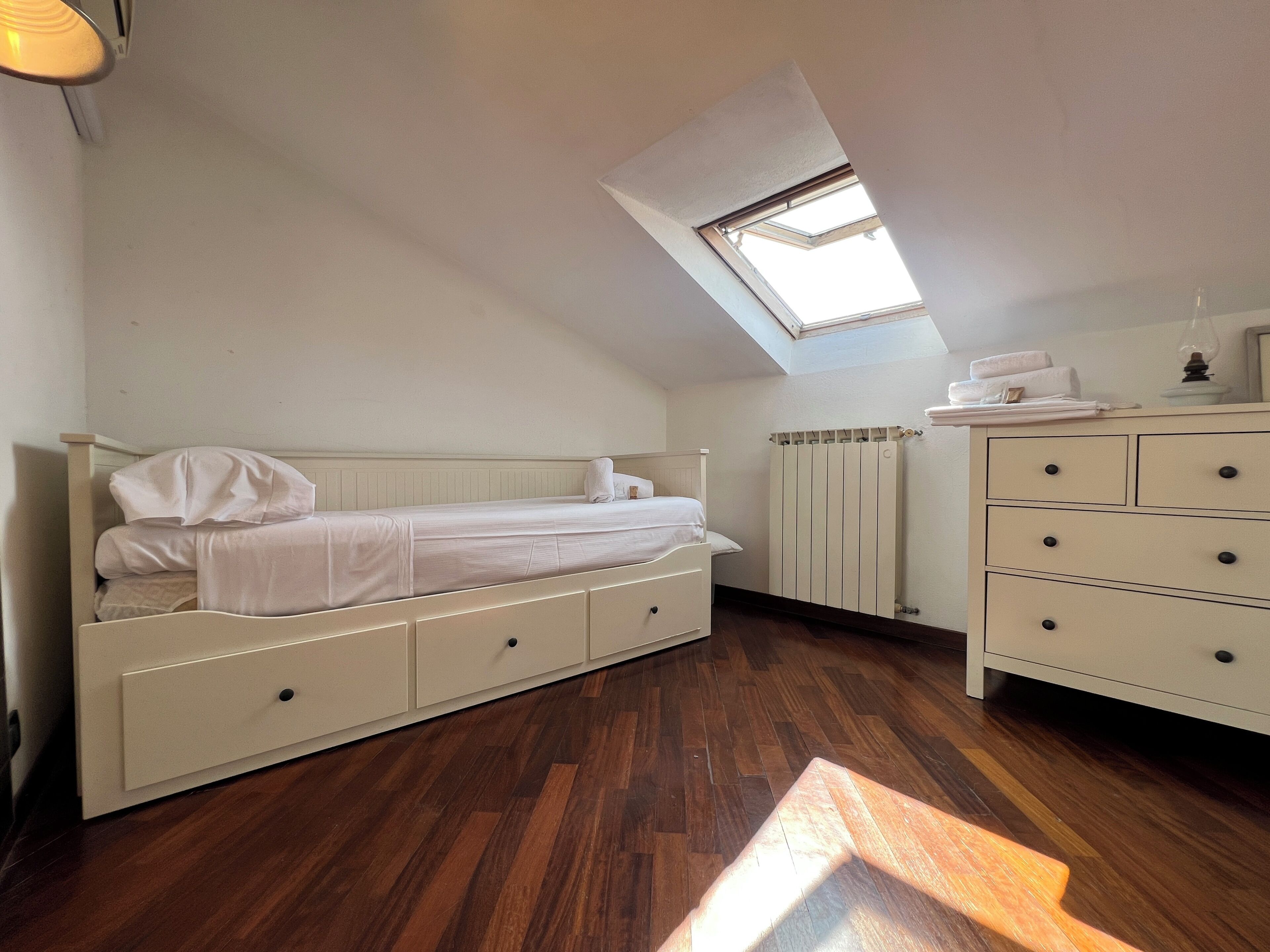 Un dormitorio con literas, cómoda, radiador y tragaluz.