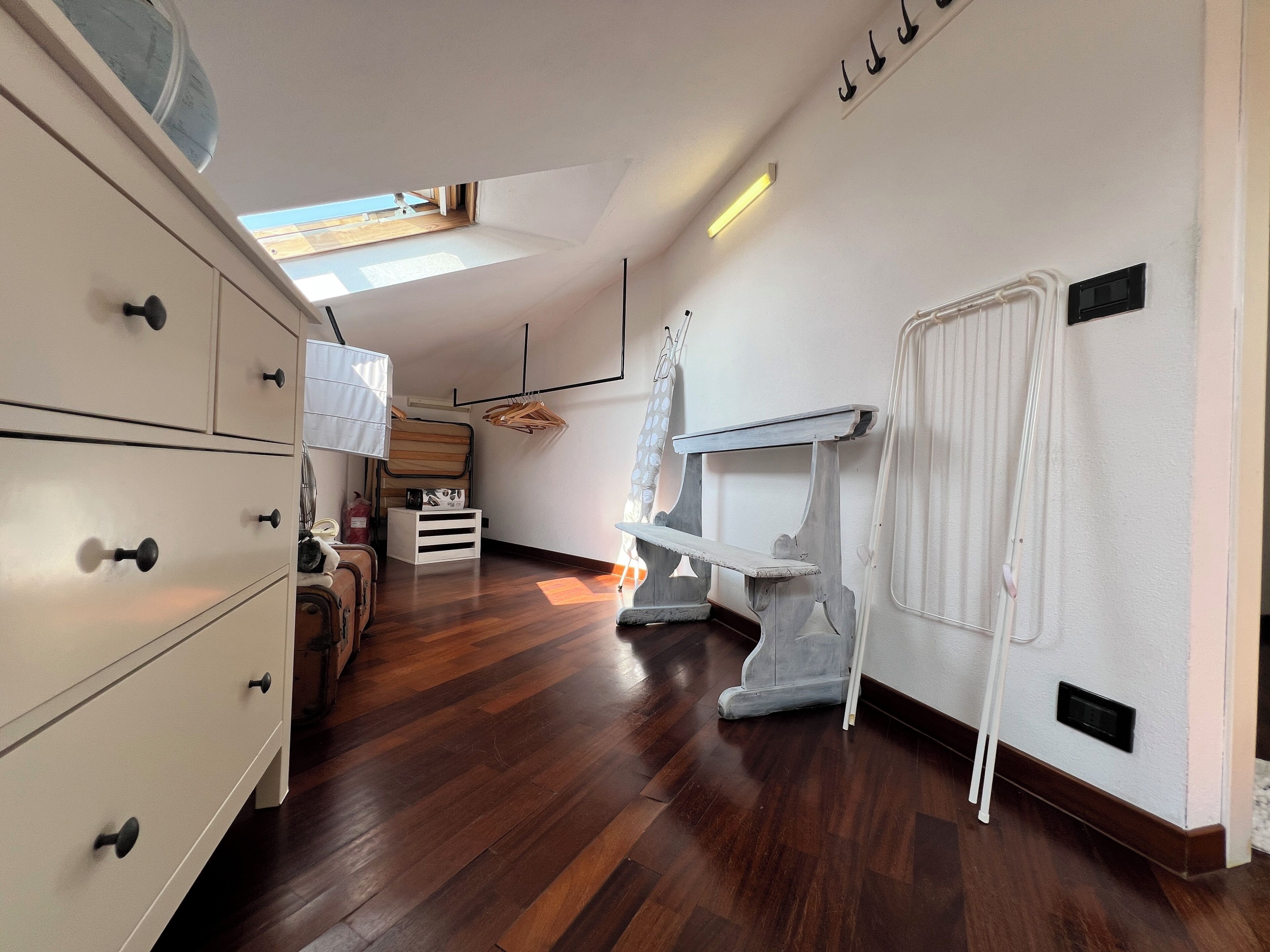 A room with a wooden floor, white walls, a white dresser, a small table, and a radiator.