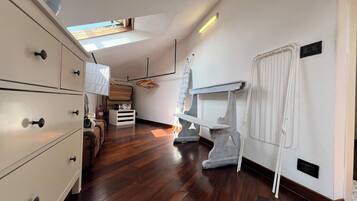 A room with a wooden floor, white walls, a white dresser, a small table, and a radiator.