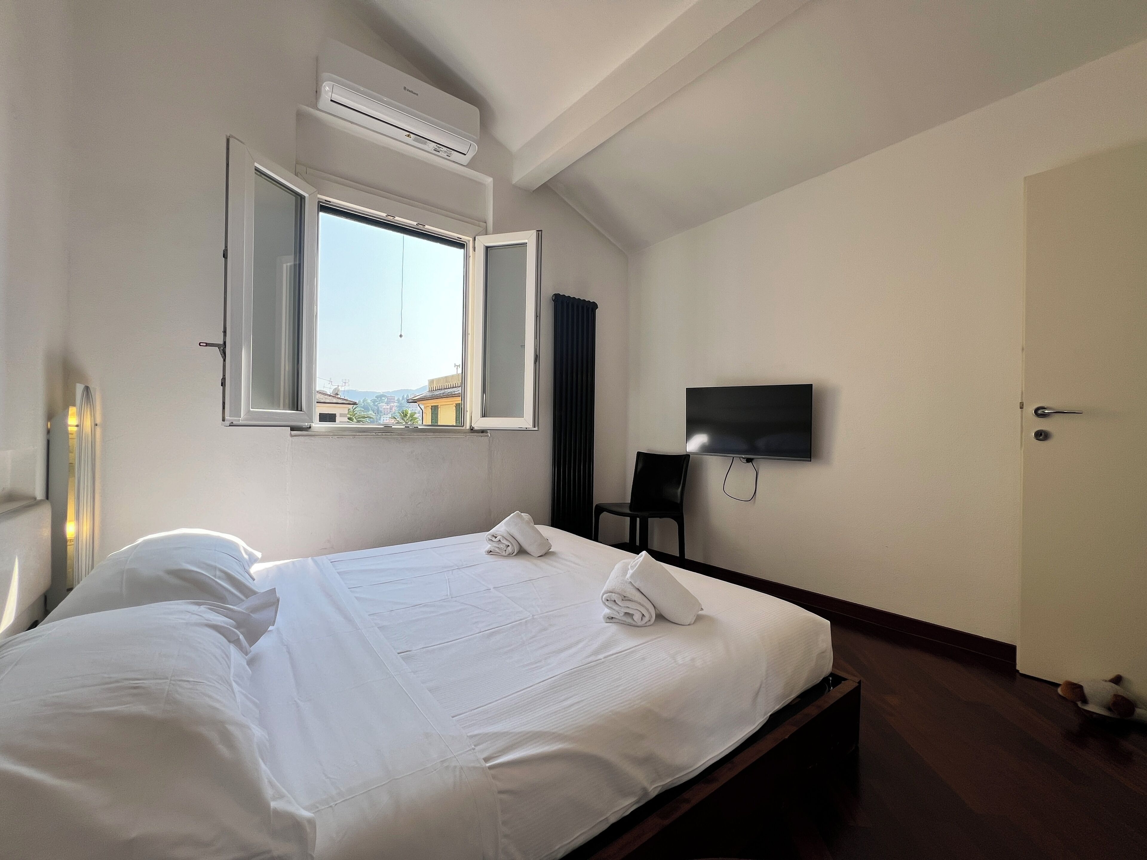 Habitación de hotel con cama, televisor de pantalla plana en la pared, ventana abierta y aire acondicionado.