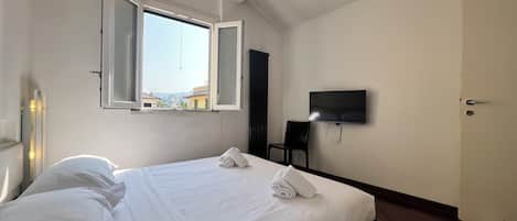 Habitación de hotel con cama, televisor de pantalla plana en la pared, ventana abierta y aire acondicionado.