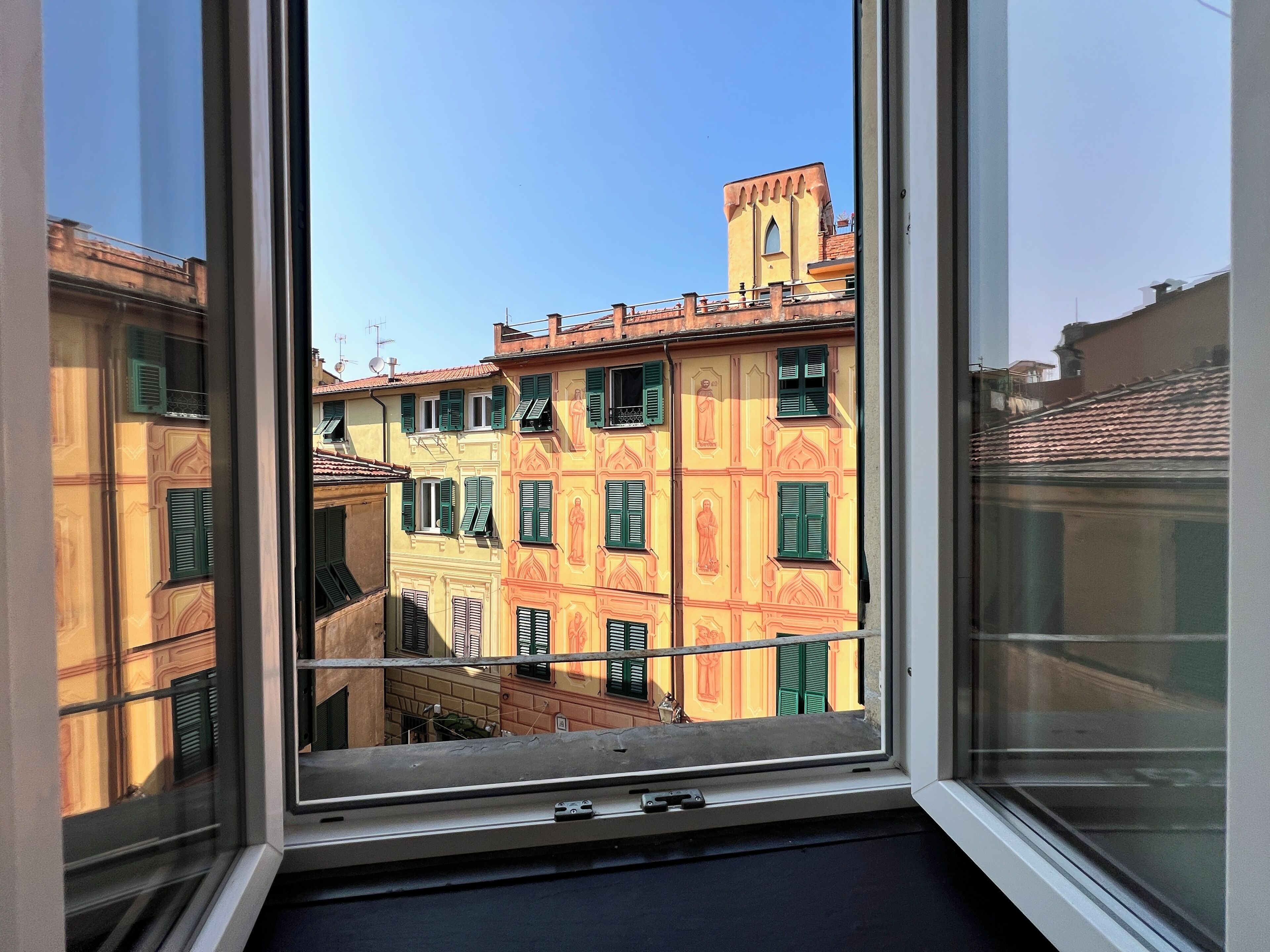 A window with a view of colorful buildings, a clear sky, and a metal railing.