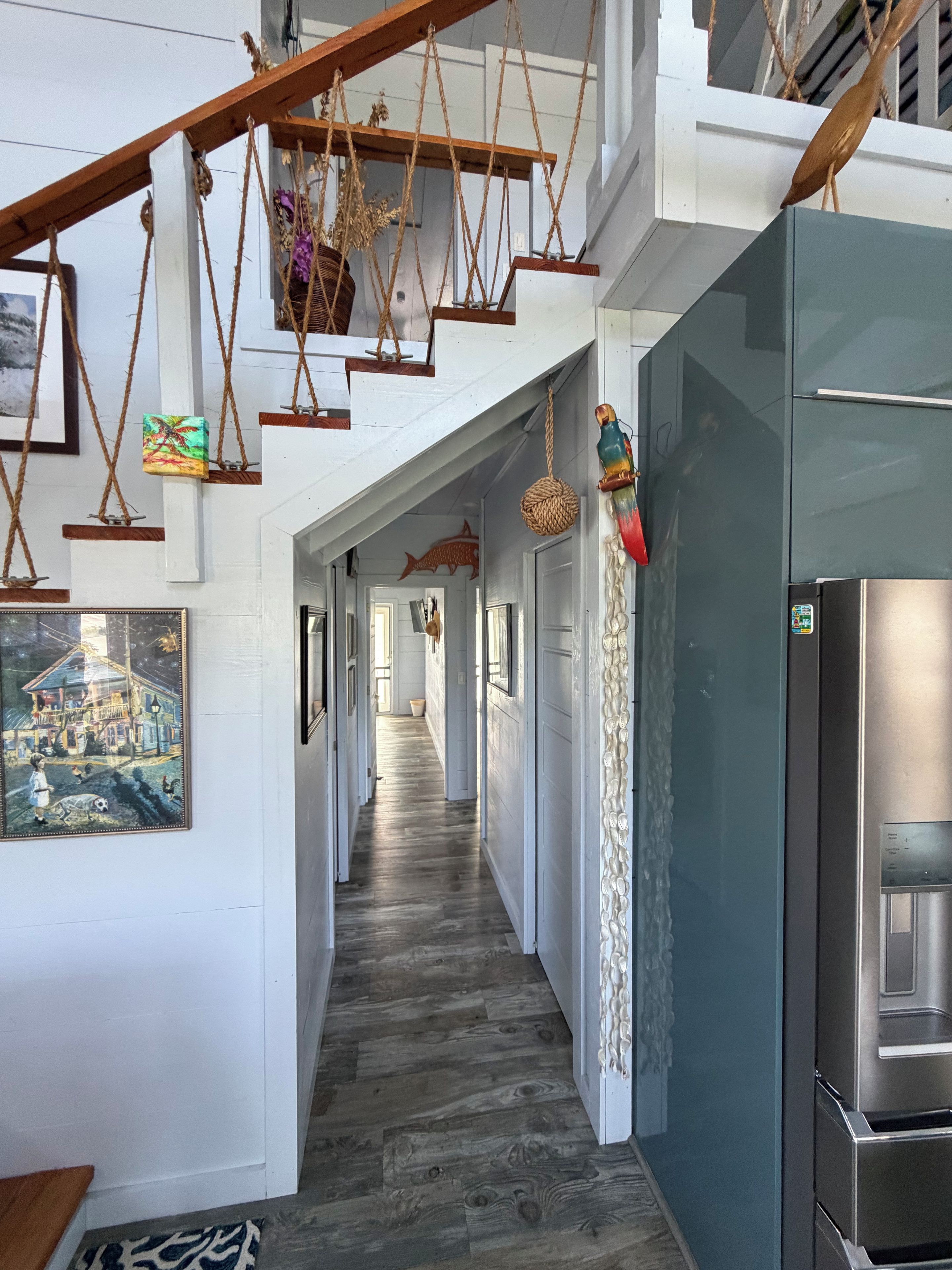 A hallway with a wooden floor, hanging decorations, and a refrigerator.
