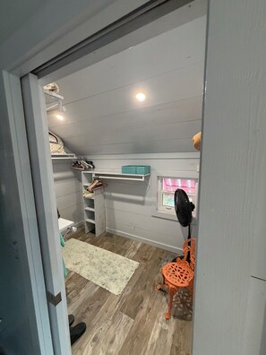 Una habitació amb lliteres, un escriptori, una cadira, un ventilador i una finestra.
