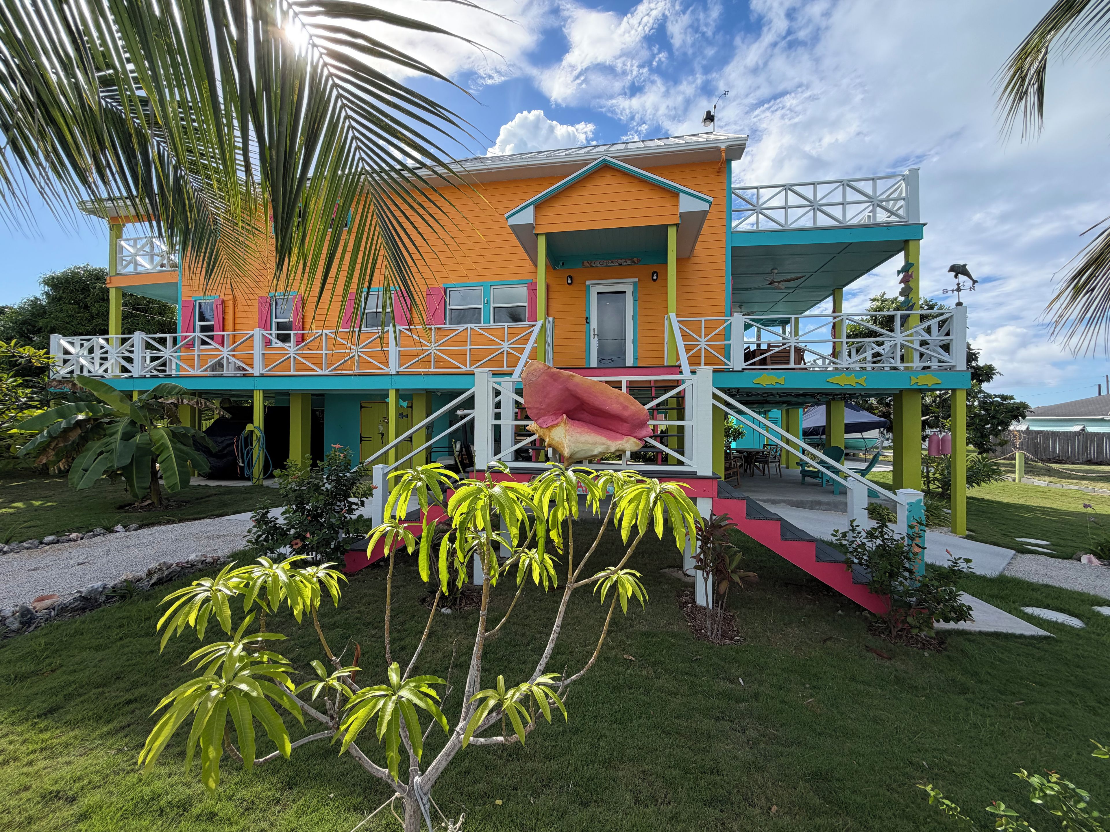 A colorful two-story building with a balcony, a staircase, and a small garden area.
