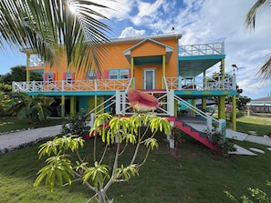 A colorful two-story building with a balcony, a staircase, and a small garden area.