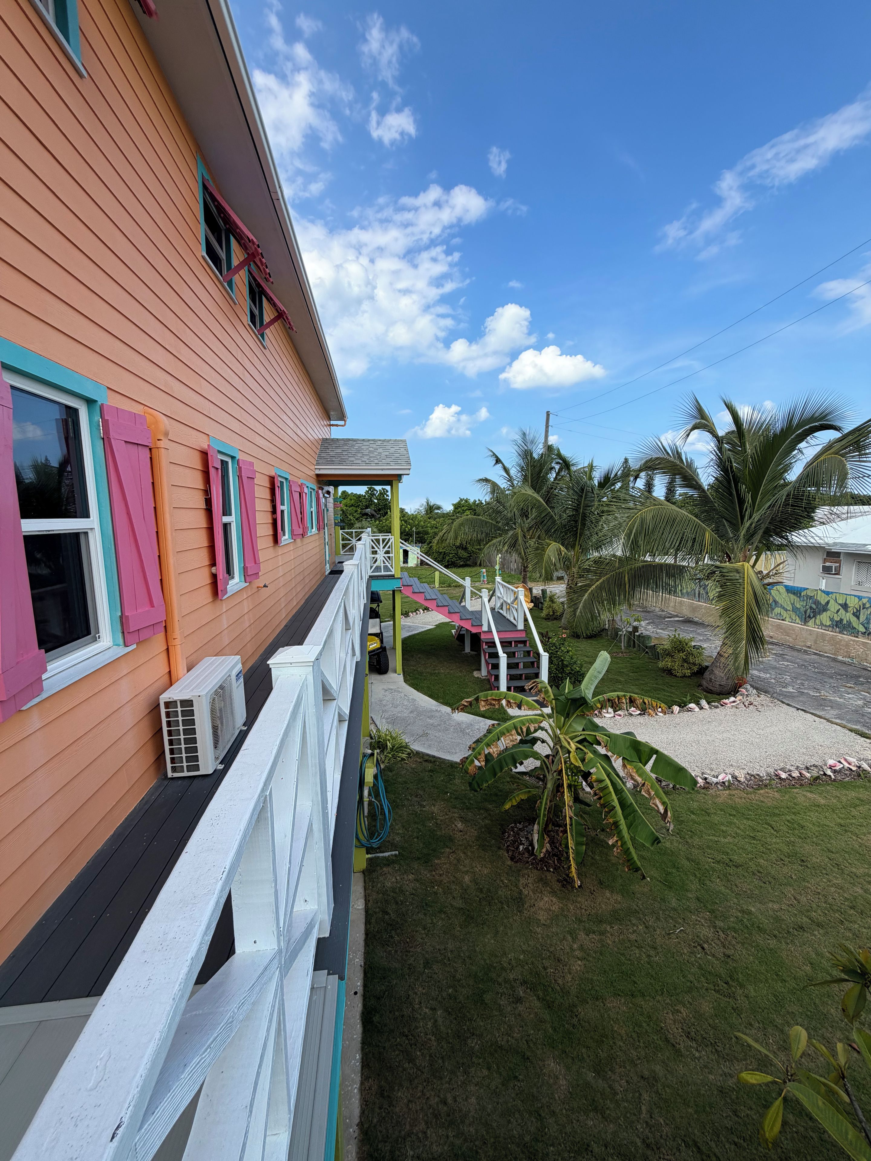 A house with a porch, a staircase, and a lawn with palm trees.
