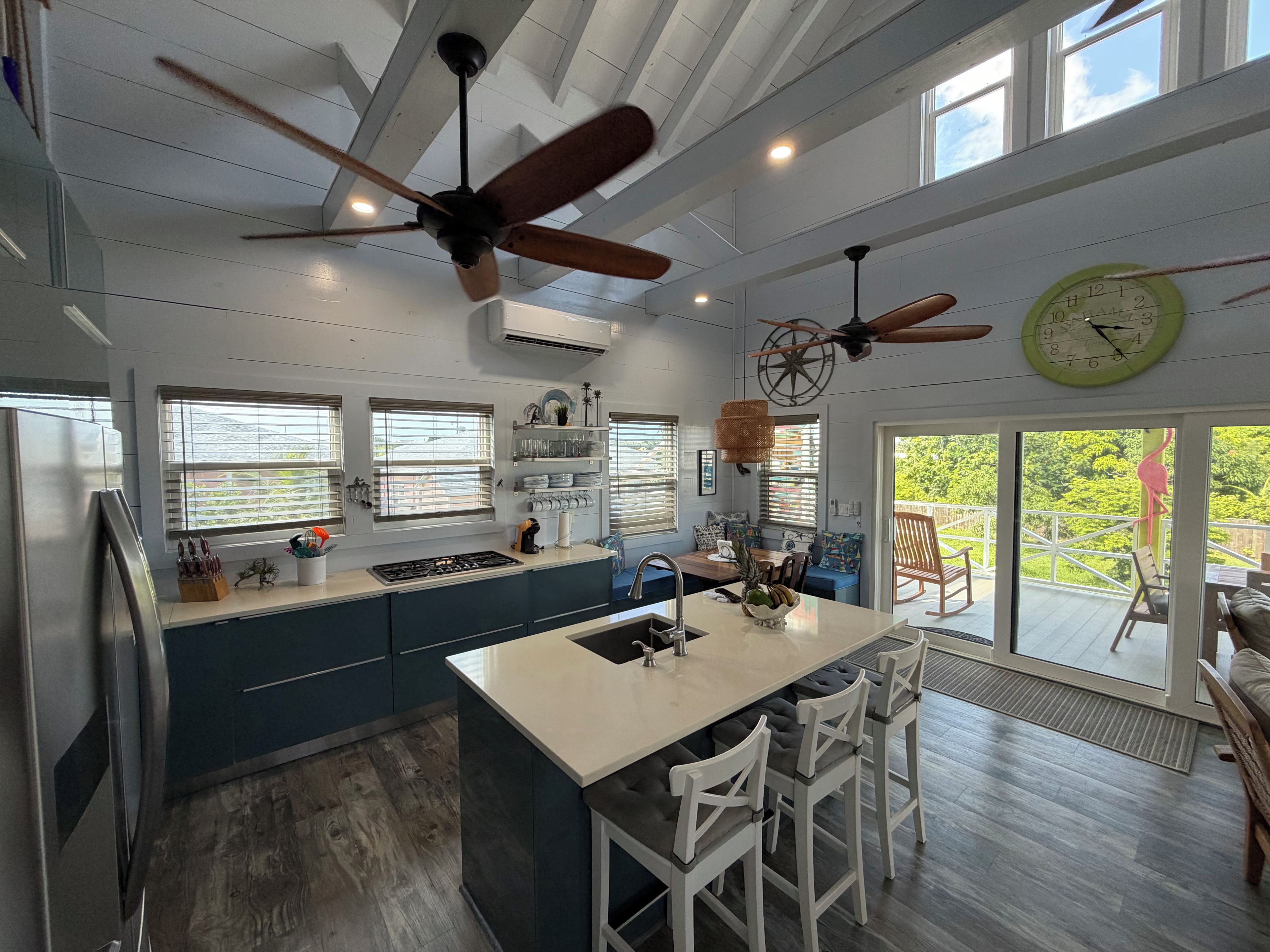 A modern kitchen with a central island, ceiling fans, and large windows.