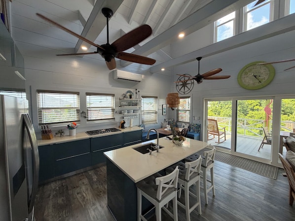 A modern kitchen with a central island, ceiling fans, and large windows.