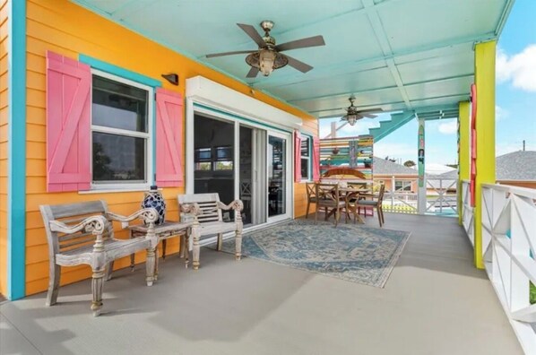 A covered porch with a ceiling fan, a dining table with chairs, and a bench.