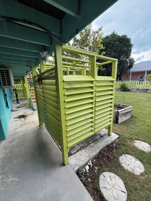 Un espacio al aire libre techado con una estructura verde, un sendero de concreto y un césped.