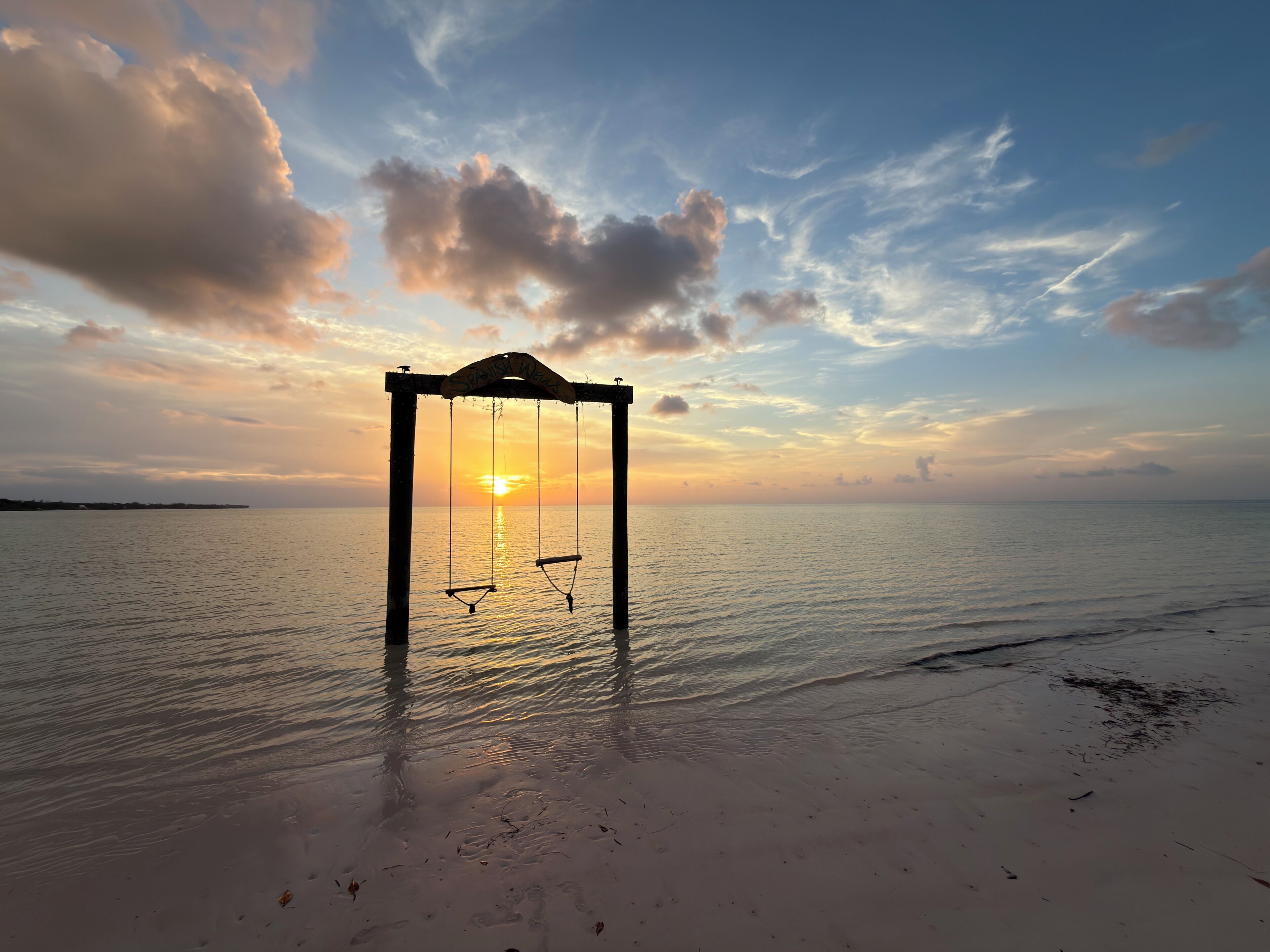 A swing set on a beach with a sunset in the background.