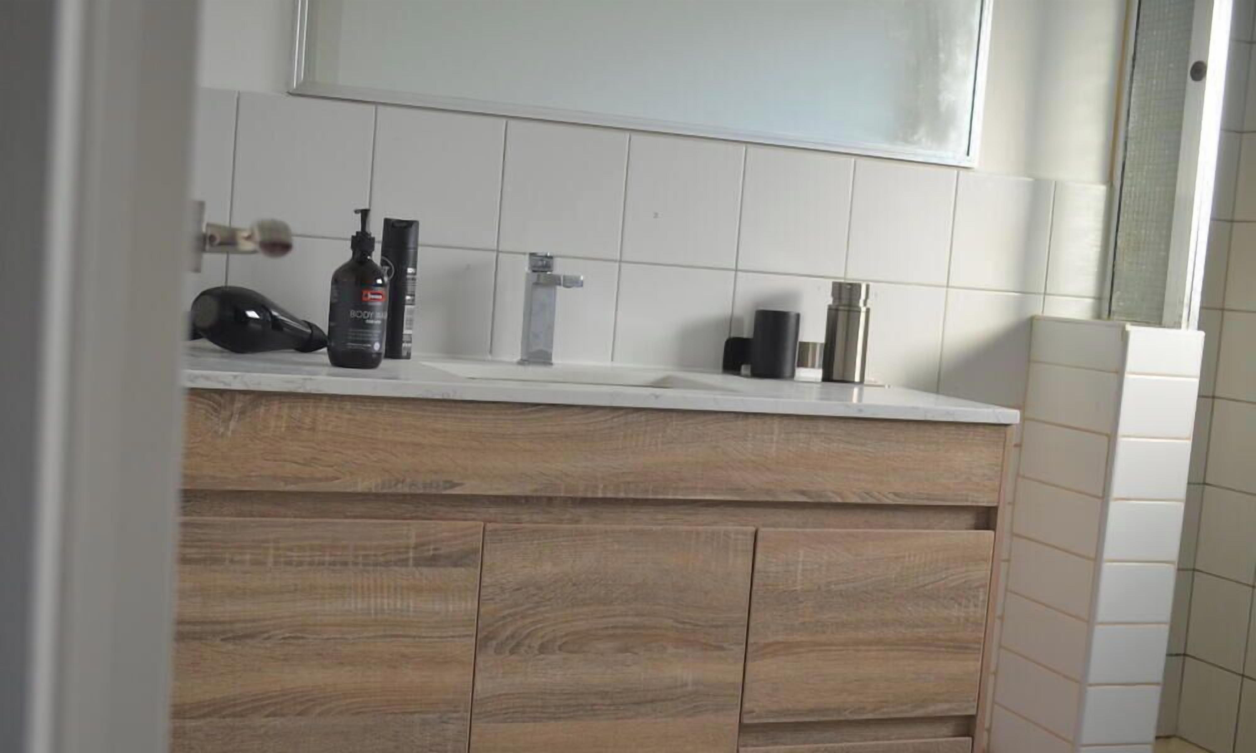 Een badkamer met een houten wastafelmeubel, een spiegel en toiletartikelen op het aanrecht.