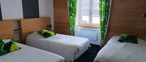 A hotel room with two beds, a wooden headboard, a white radiator, and a window with green curtains.
