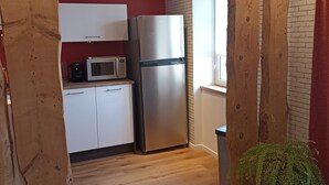 A compact kitchen with white cabinets, a stainless steel refrigerator, a microwave, and a potted fern.