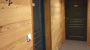 A hallway with wooden walls, a door with a nameplate, and a wall-mounted light fixture. - Beautiful Apartment in the Heart of Les Rousses Village (Les Rousses)