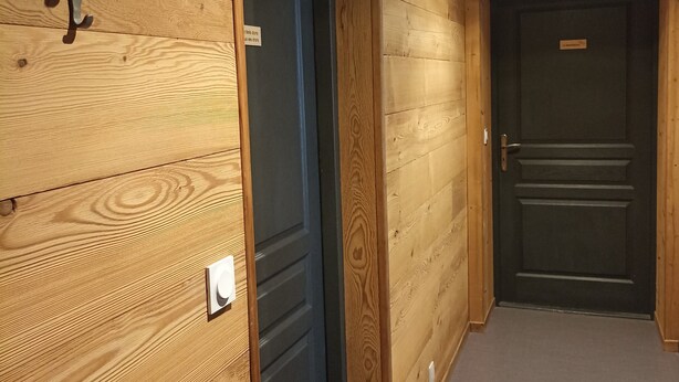 A hallway with wooden walls, a door with a nameplate, and a wall-mounted light fixture.