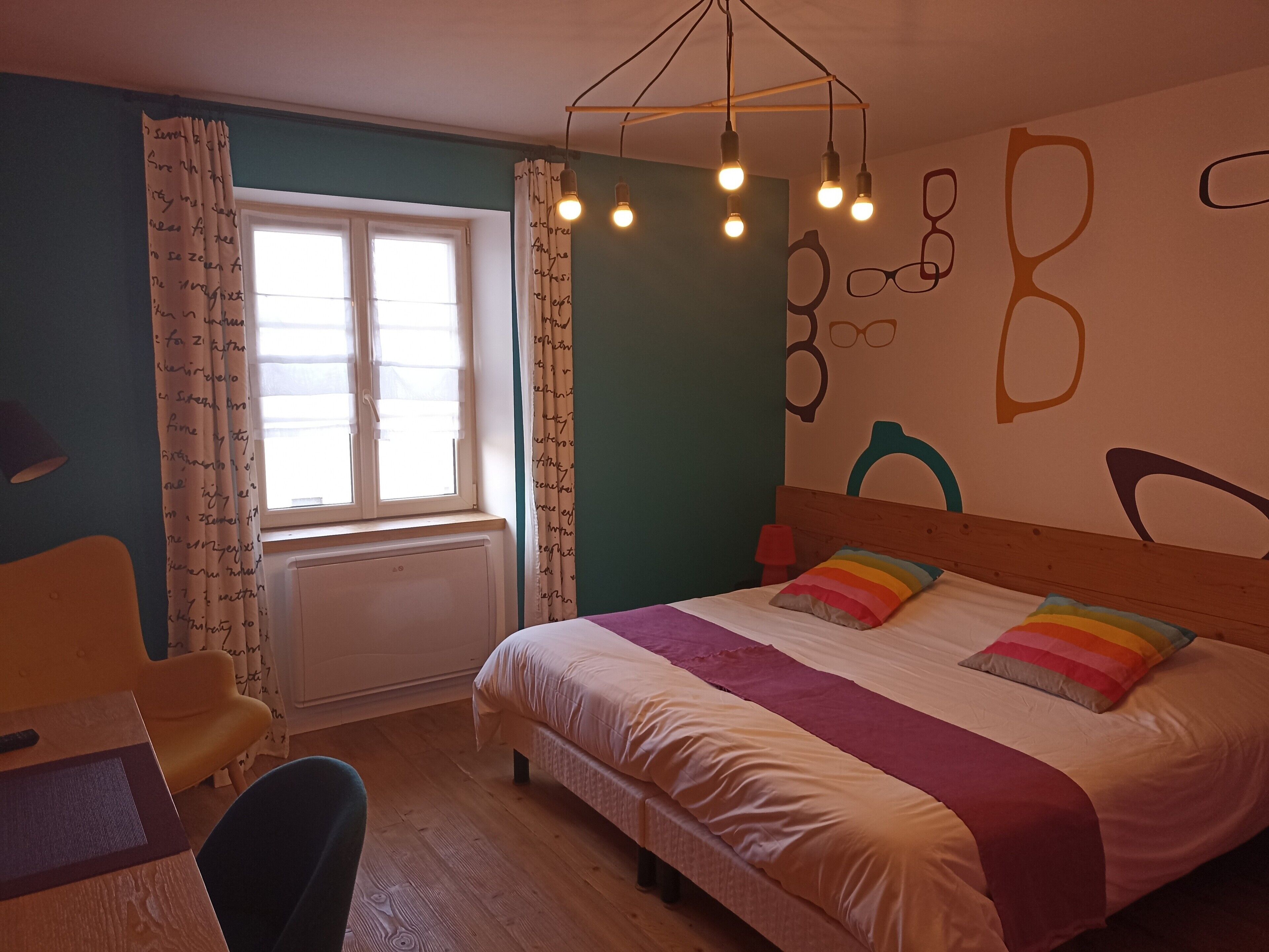 A bedroom with a bed, a chair, a window, and a wall with abstract designs.