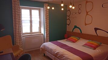 A bedroom with a bed, a chair, a window, and a wall with abstract designs.