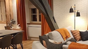 A modern living room with a sofa, dining table, chairs, and a brick wall. - Beautiful Apartment in the Heart of Les Rousses Village (Les Rousses)