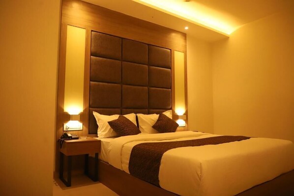 Habitación de hotel con una cama grande, cabecera con diseño acolchado, lámparas de noche y mesita de noche con un teléfono.