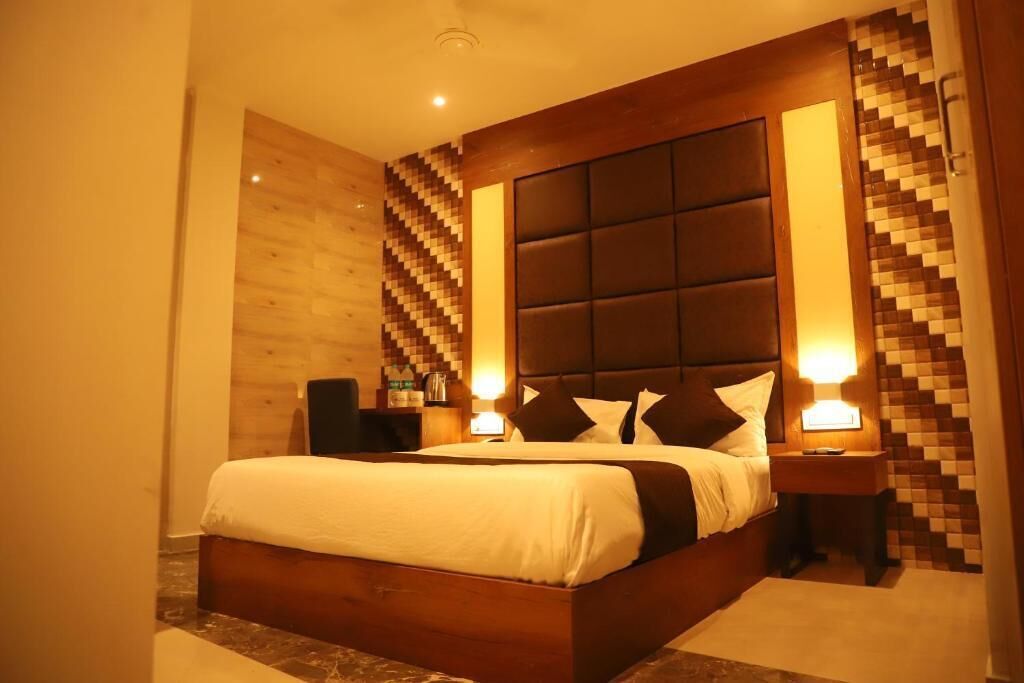 Habitación de hotel con una cama grande, cabecera de madera, mesita de noche y una pared con diseño geométrico.