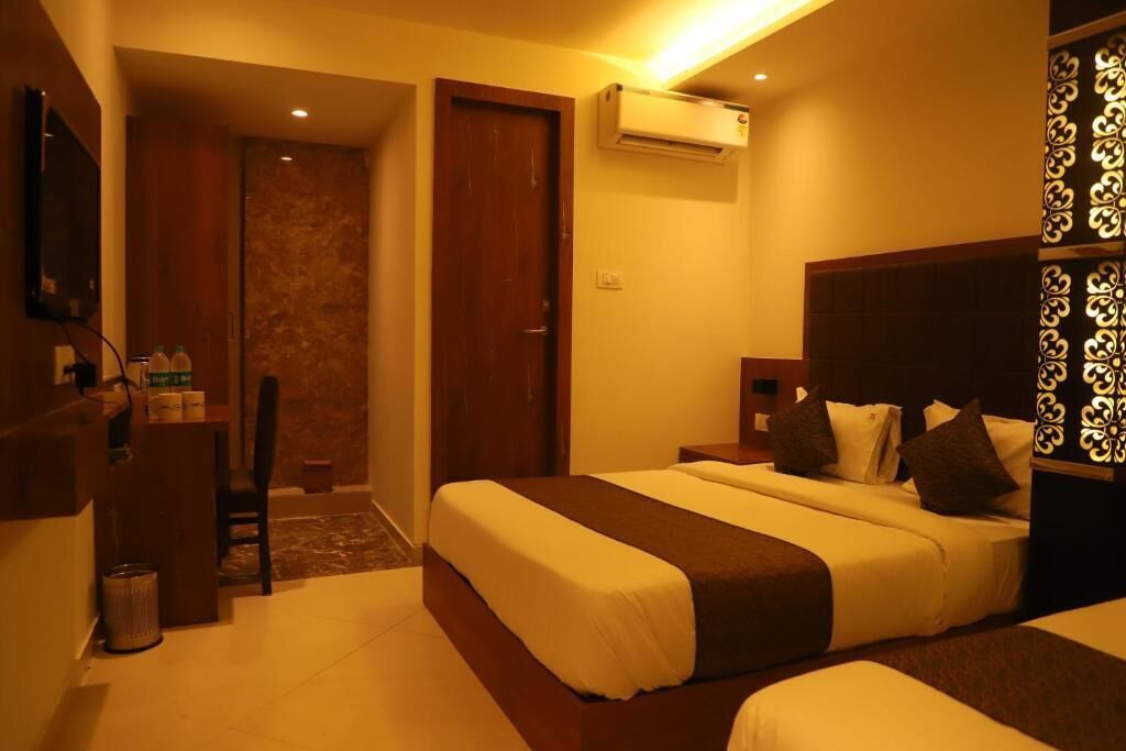 A hotel room with a bed, bedside tables, a desk with a chair, an air conditioning unit, and a decorative wall panel.