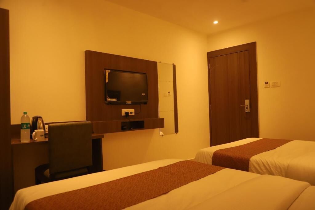 Habitación de hotel con dos camas, un televisor montado en la pared, un escritorio con una silla y una puerta.