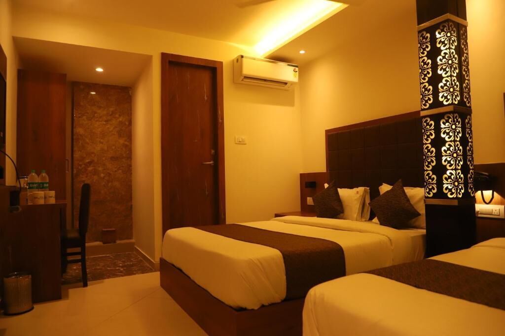 Quarto de hotel com duas camas, uma escrivaninha, uma cadeira, unidade de ar condicionado e um painel decorativo.