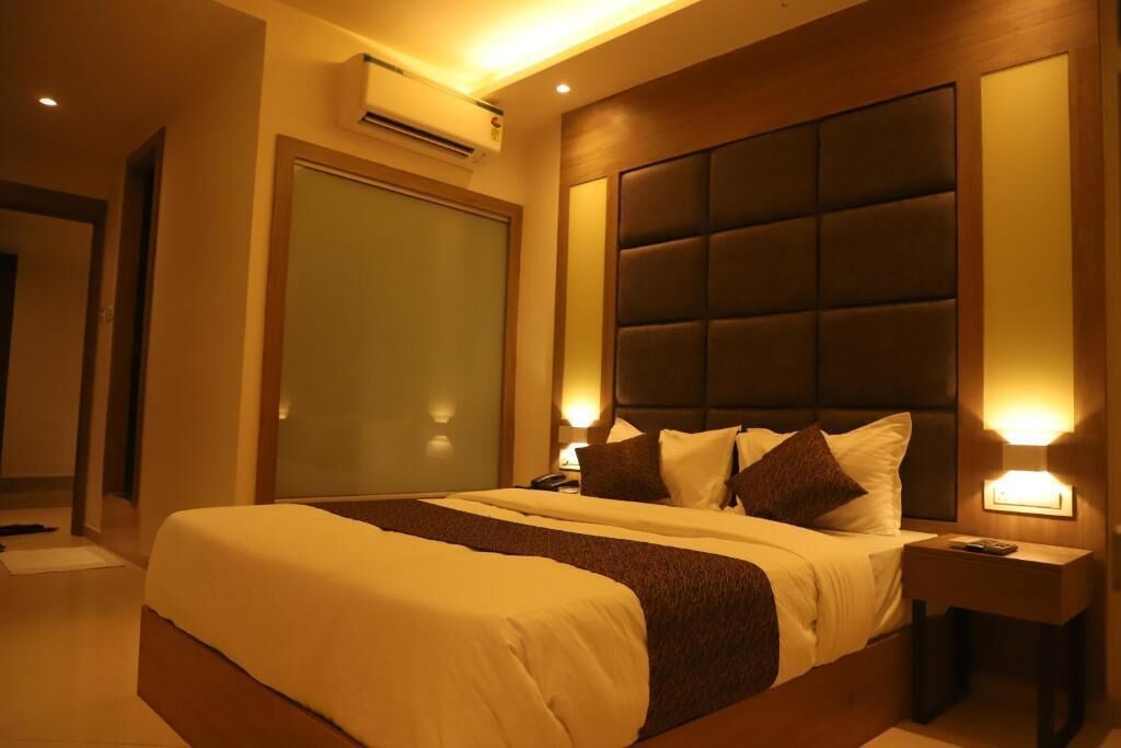 Een hotelkamer met een groot bed, een hoofdeinde met een zachte rugleuning, een nachtkastje met een lamp en een airconditioning op de muur.